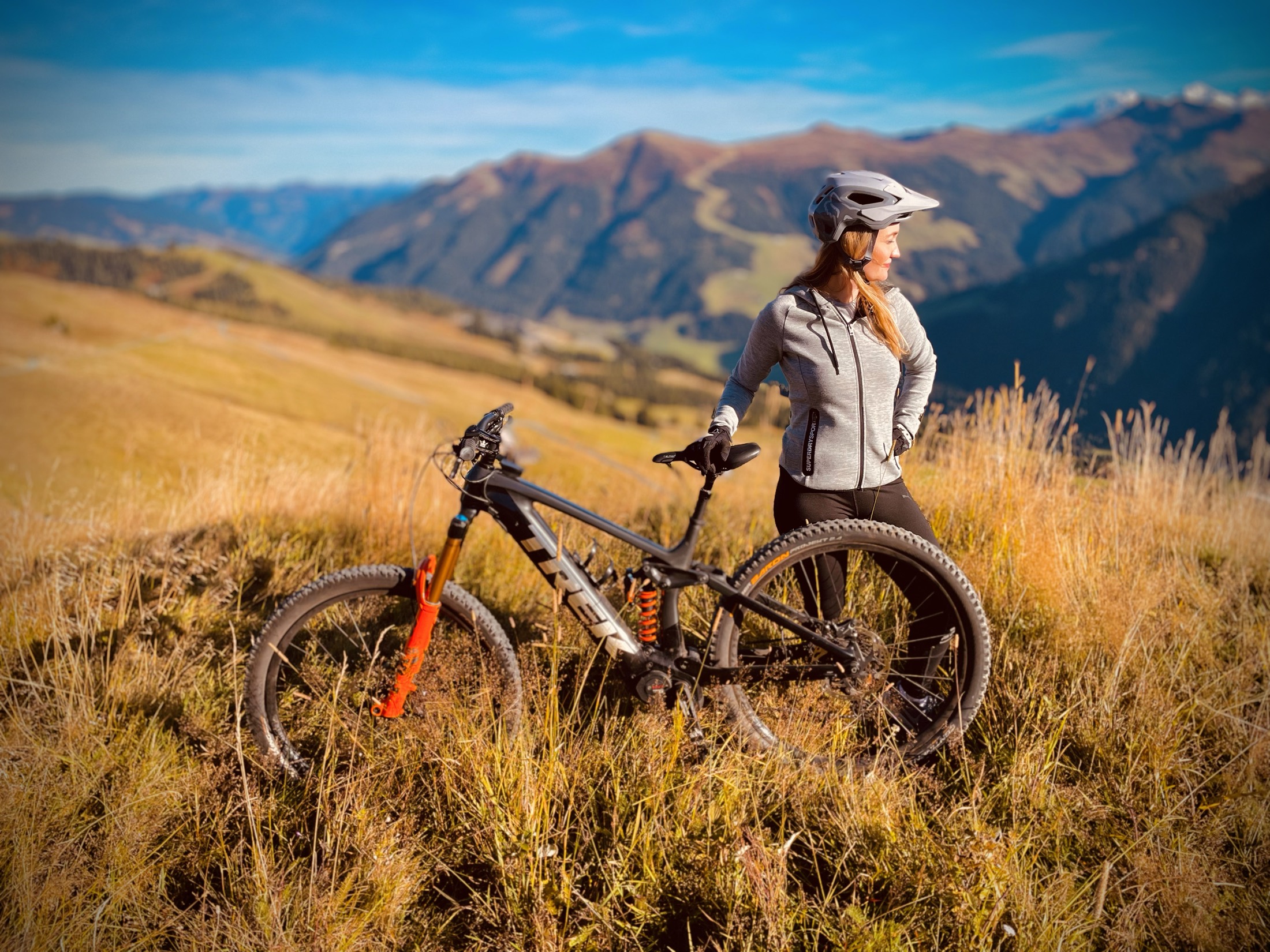 Fahrerin mit E-MTB in einer goldenen Almwiese vor Bergpanorama